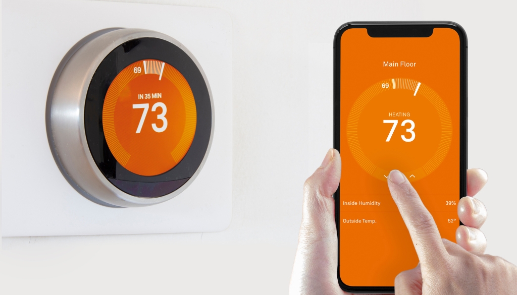 A smart thermostat on the wall with a finger controlling the temperature from an iPhone.