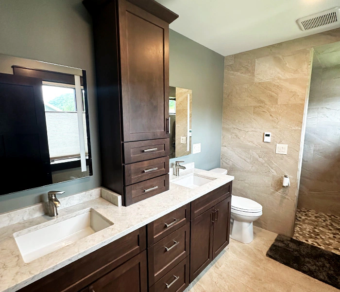 Remodeled bathroon with dual sinks, dark cabinetry, and walk-in shower.