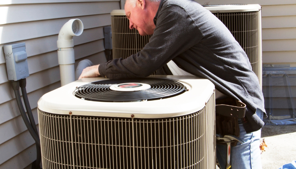 Man repairing an air conditioning unit outside of a residential home.