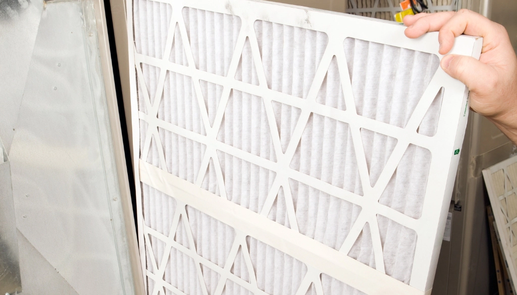 Person replacing a MERV 8 pleated HVAC filter in a home heating and cooling system to improve indoor air quality.