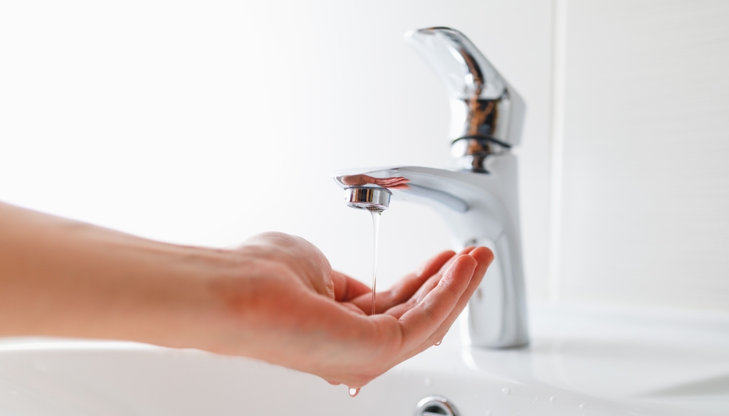 Hand under a running sink faucet with low water pressure.