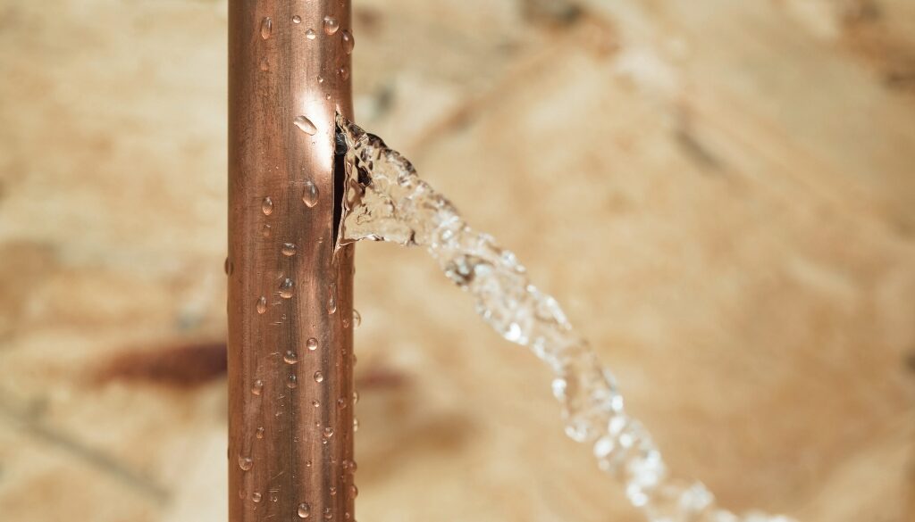 A close up of a burst copper pipe leaking water.