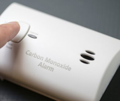 A close-up of a finger about to push a button on a carbon monoxide alarm.