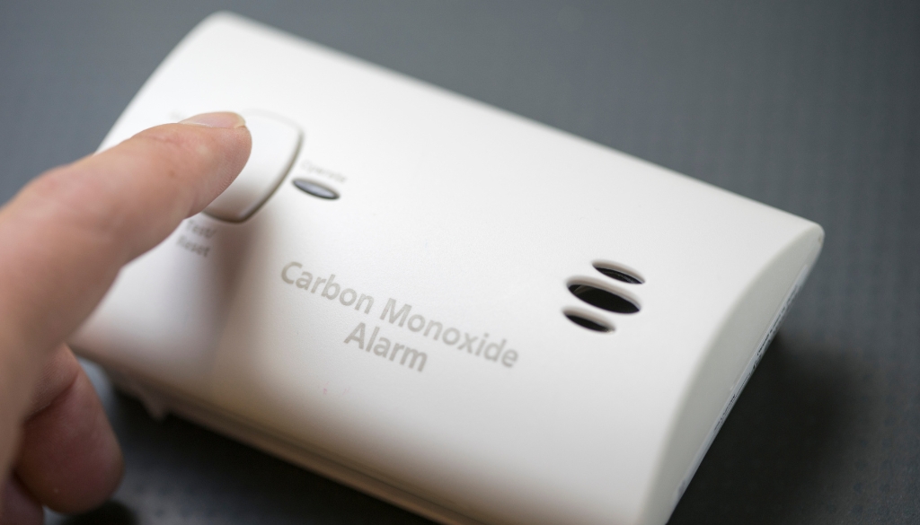 A close-up of a finger about to push a button on a carbon monoxide alarm.