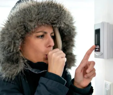 A woman in her winter coat cranking the thermostat up, which is a common heating mistake in winter.