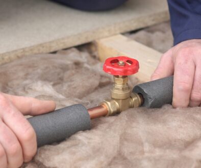 Hands insulating exposed plumbing pipes to prevent freezing and burst pipes during the fall and winter months.