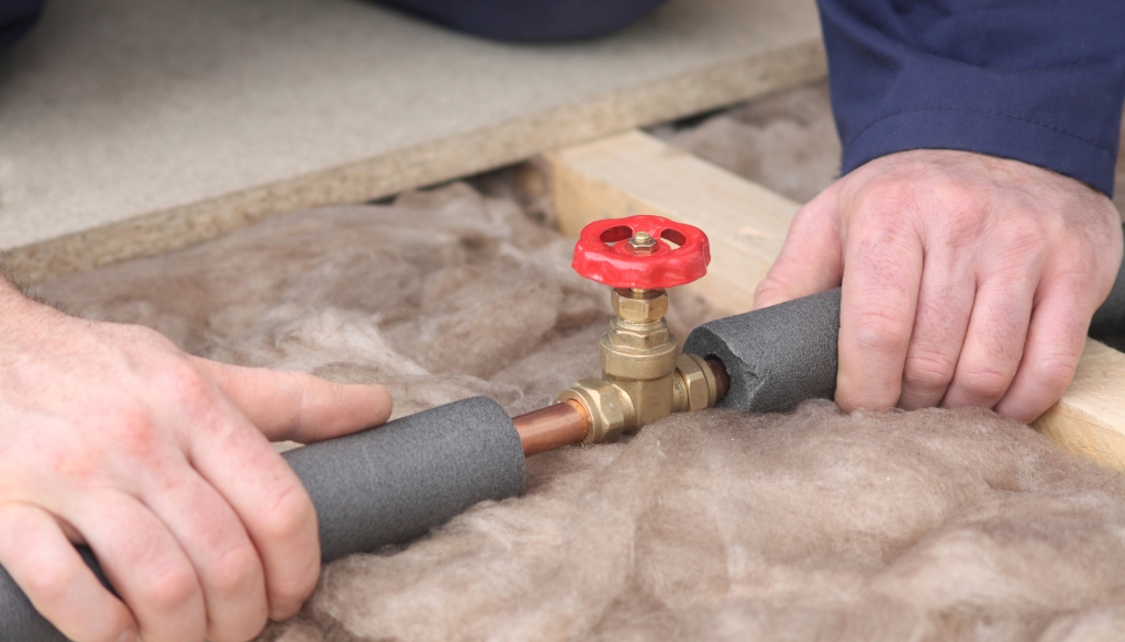 Hands insulating exposed plumbing pipes to prevent freezing and burst pipes during the fall and winter months.