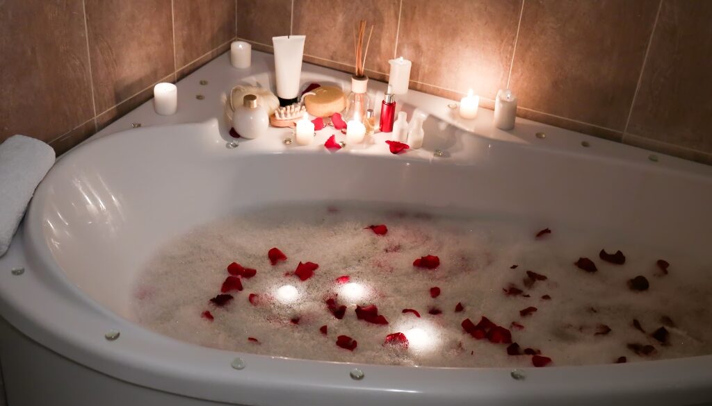 A luxurious bathtub filled with warm, bubbly water and scattered rose petals, surrounded by candles and spa essentials.