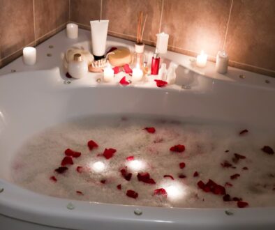 A luxurious bathtub filled with warm, bubbly water and scattered rose petals, surrounded by candles and spa essentials.