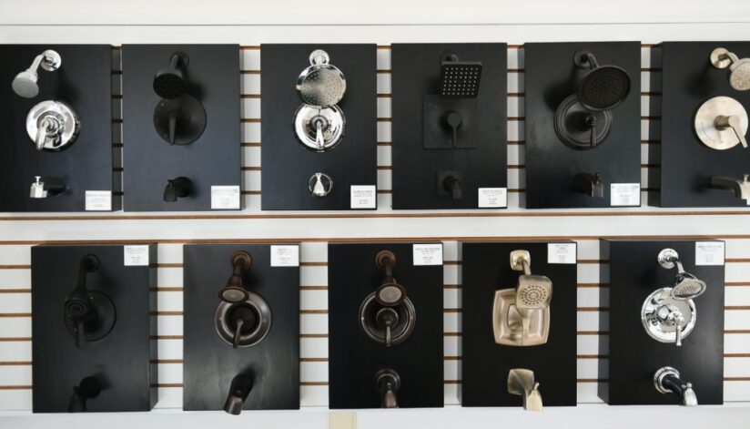 A display of various showerheads and faucet fixtures mounted on black panels in Niebuhr's showroom in La Crosse, Wisconsin, featuring brands like Kohler, Moen, and Pulse.