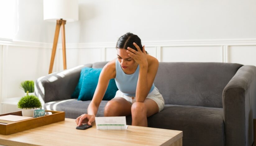 A concerned woman reviews a high energy bill while adjusting her air conditioner.