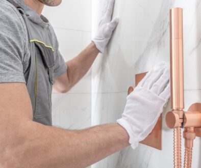 A professional contractor aligning marble wall tiles during a bathroom shower remodel, featuring a modern copper shower fixture.