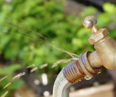 A leaking outdoor faucet with water spraying from a cracked hose connection.