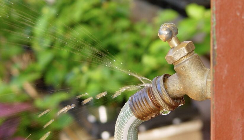 A leaking outdoor faucet with water spraying from a cracked hose connection.