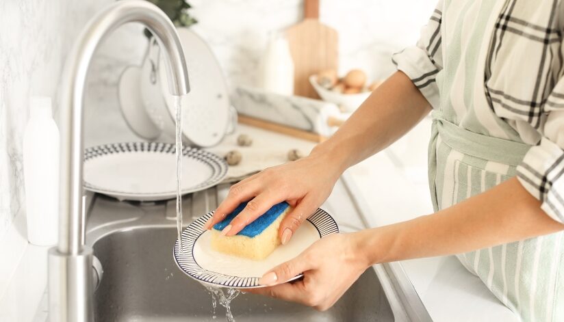 A person washing a plate at a kitchen sink with softened water and a sponge.
