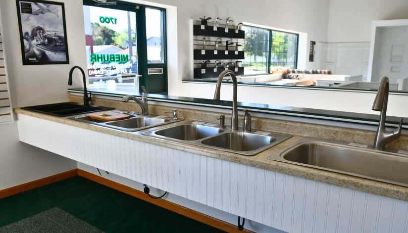 Multiple Kohler kitchen faucets and stainless steel sinks displayed on a long countertop inside the Niebuhr Plumbing showroom in La Crosse, Wisconsin.