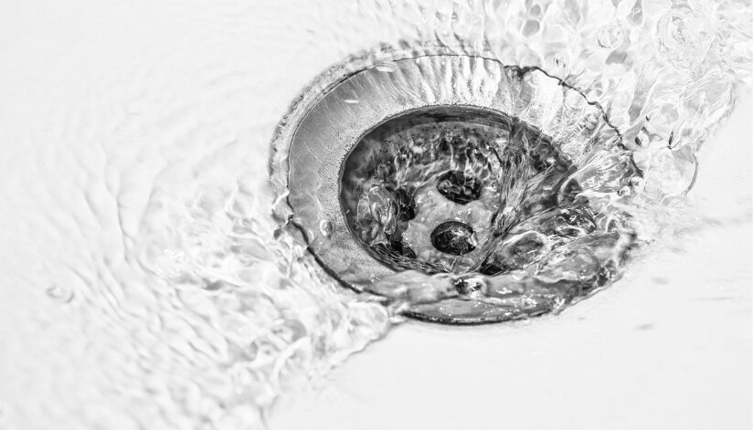 A silver drain in a white sink with clear water draining through it.