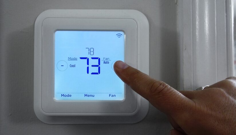 A hand adjusting a wall-mounted smart thermostat set to 73 degrees, displaying cooling mode and fan settings on a digital screen.