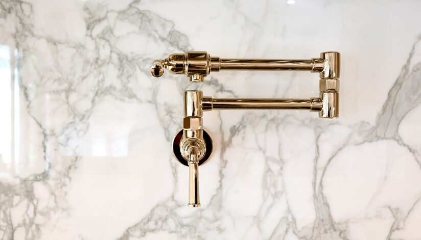A gold-finish pot filler faucet on a marble kitchen wall.