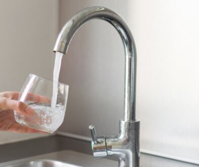 A person's hand holding a glass under a kitchen faucet that is being filled with water.