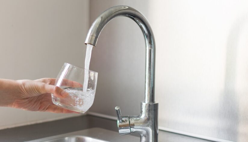 A person's hand holding a glass under a kitchen faucet that is being filled with water.