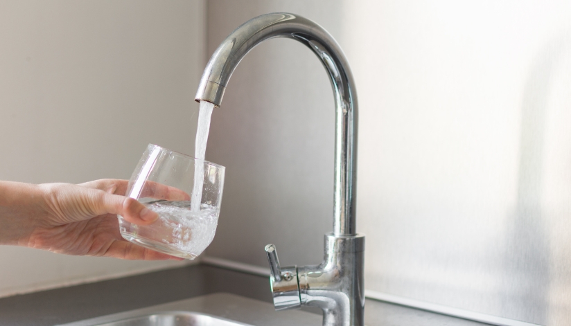 A person's hand holding a glass under a kitchen faucet that is being filled with water.