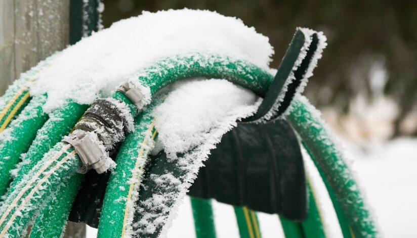 Snow-covered garden hose left connected outdoors after plumbing winterization was forgotten.